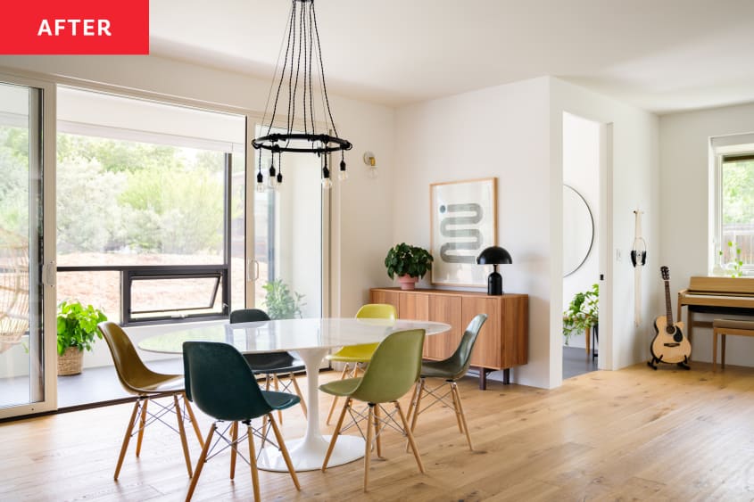 Dining room after renovation. Wood floors, large round white dining table with mid century style green chairs, modern chandelier light overhead. Wood credenza with plant and small black lamp. Piano and guitar