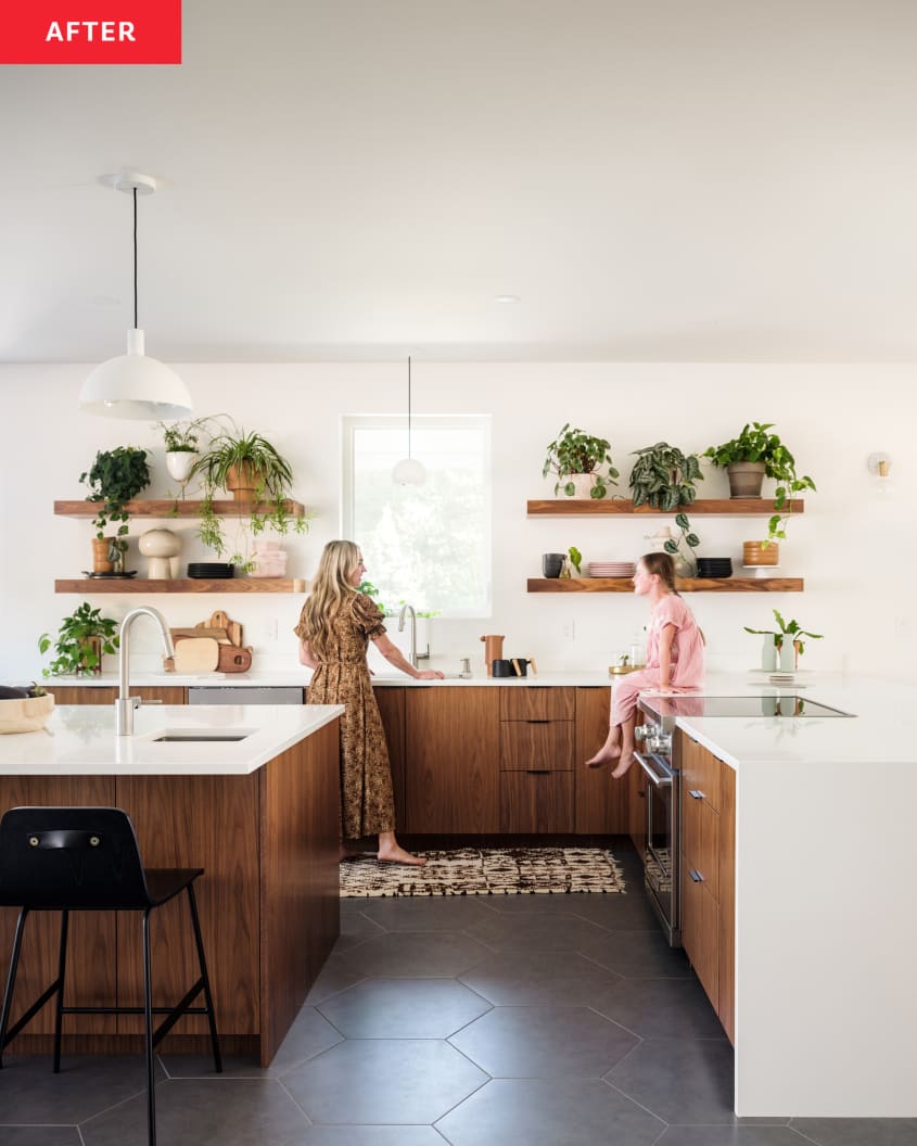 woman and daughter in kitchen after renovation. lots of white, wood. Wood floating shelves with lots of plants