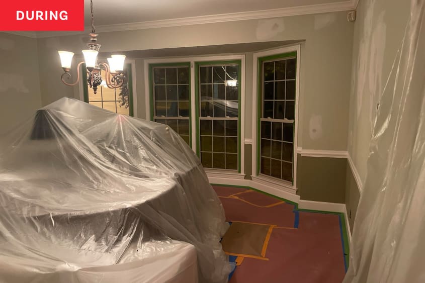 Photo of room during transformation into home office: furniture is covered by a plastic tarp and painting of walls/trim has started