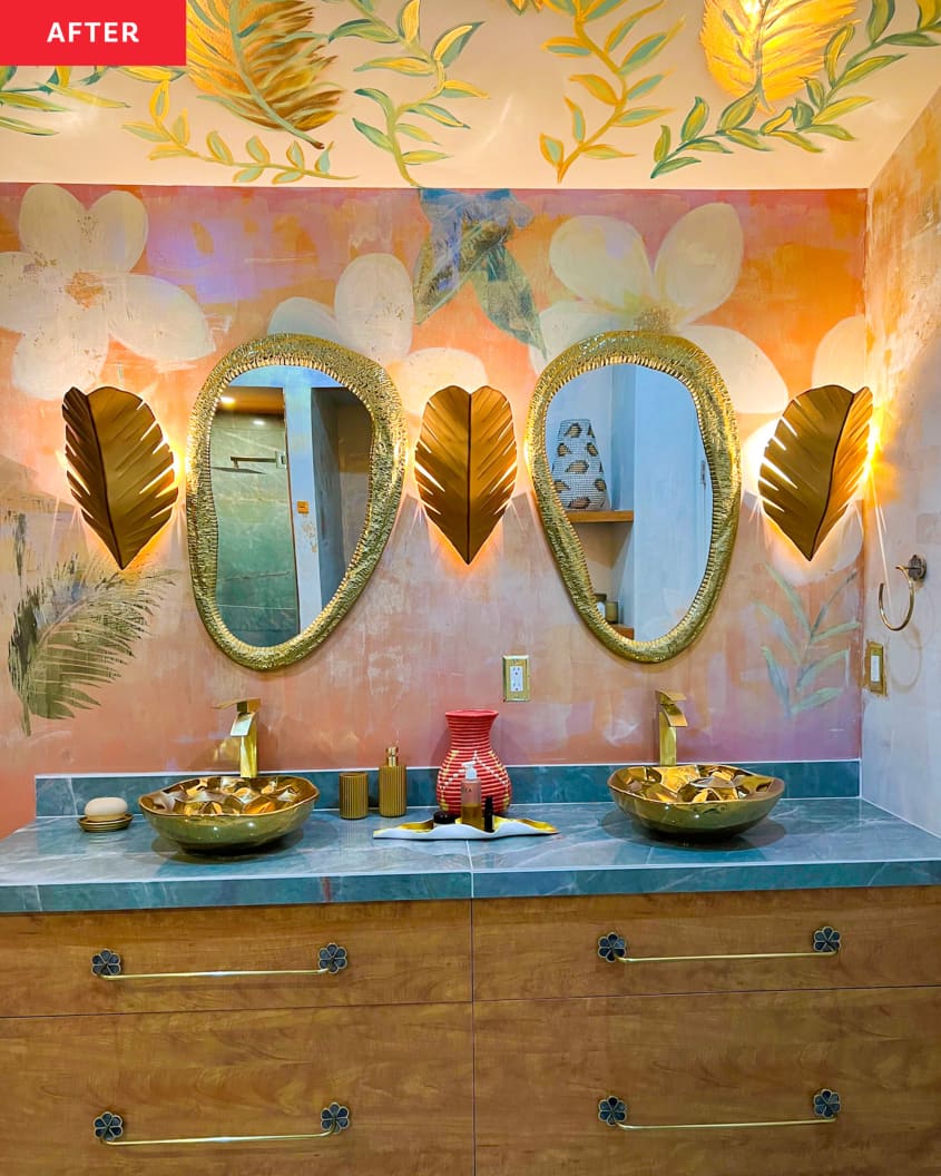 Bathroom after renovation with tropical theme. Walls painted with leaves, flowers, feathers in shades of golds, pinks, greens, leaf motif pendant light, hardware in shades of gold, freestanding white bathtub, gold patterned double basin sinks, gold framed mirrors, painted hex tiles on floor and on walls