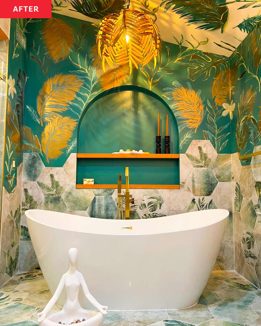 Bathroom after renovation with tropical theme. Walls painted with leaves, flowers, feathers in shades of golds, pinks, greens, leaf motif pendant light, hardware in shades of gold, freestanding white bathtub, gold patterned double basin sinks, gold framed mirrors, painted hex tiles on floor and on walls
