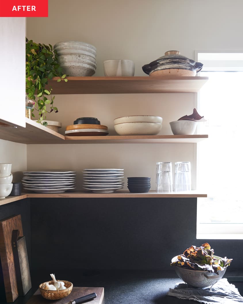 Open shelves in kitchen filled with ceramic dish ware and a dark backsplash below shelving.