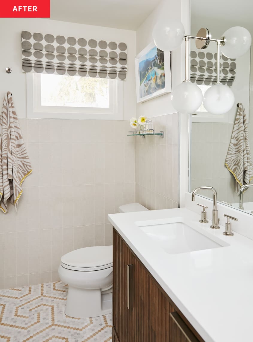 Bathroom after renovation/makeover: modern wood sink cabinet, white countertops, dual sinks, 2 globe sconces, silver hardware, mosaic pattern tile floor, white tile and white walls