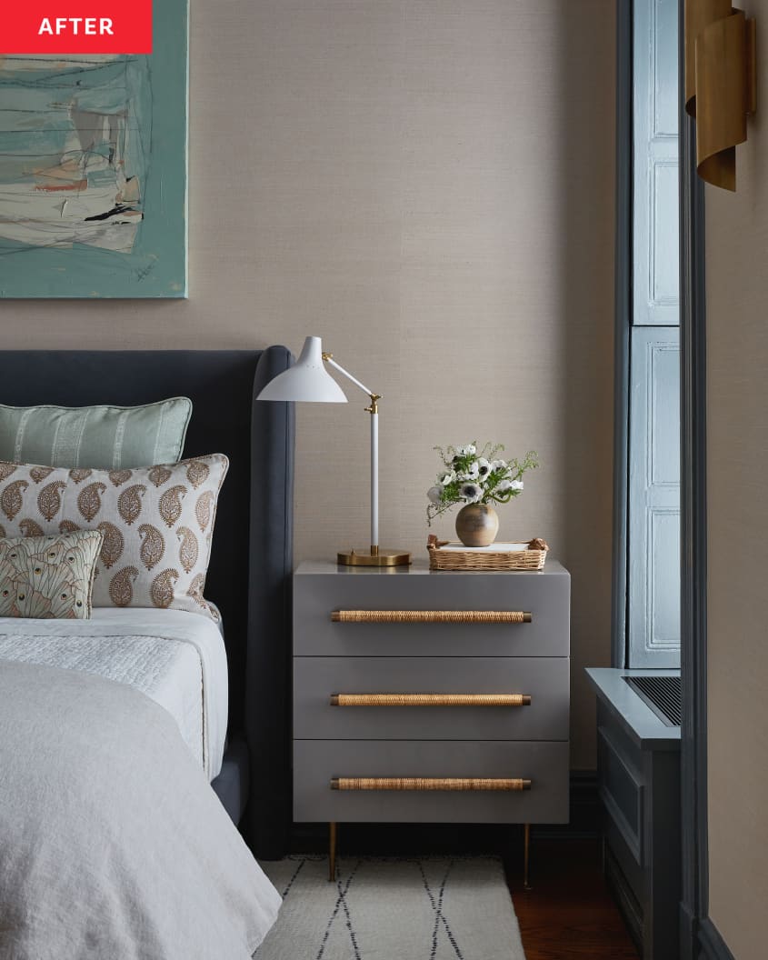White task lamp and small bud vase arrangement sit on top of grey nightstand with woven grass handles in newly renovated bedroom.