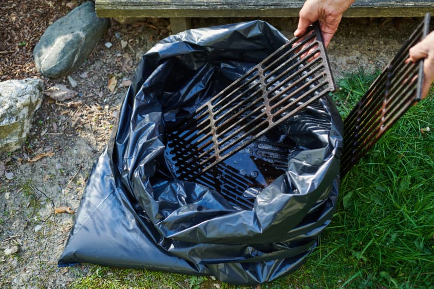 taking grill grates out of trash bag filled with cleaning solution