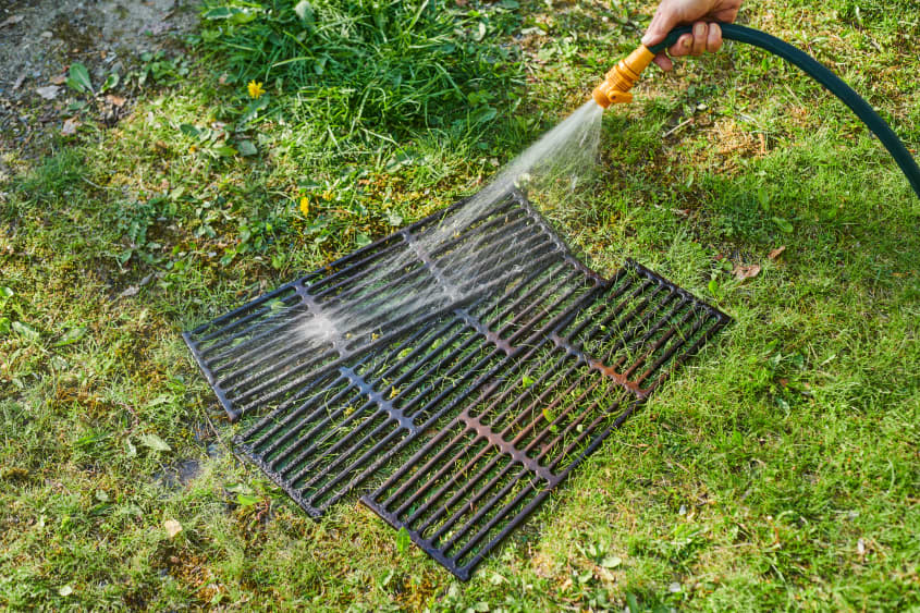 spraying down grill grates with a hose in backyard