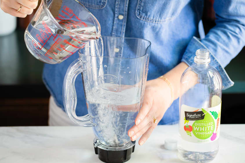 Blender cavity filled halfway with white vinegar, pouring in water to fill the rest