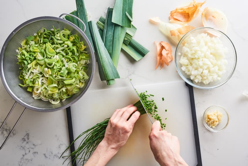 cutting chives on a cutting board with other prepped ingredients