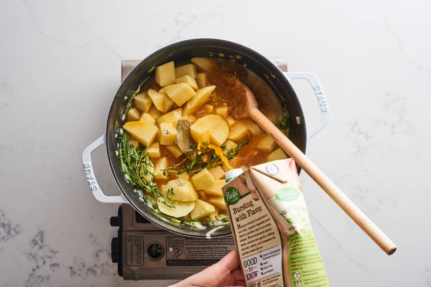 adding chicken broth to dutch oven with potatoes, leeks, onions and other ingredients