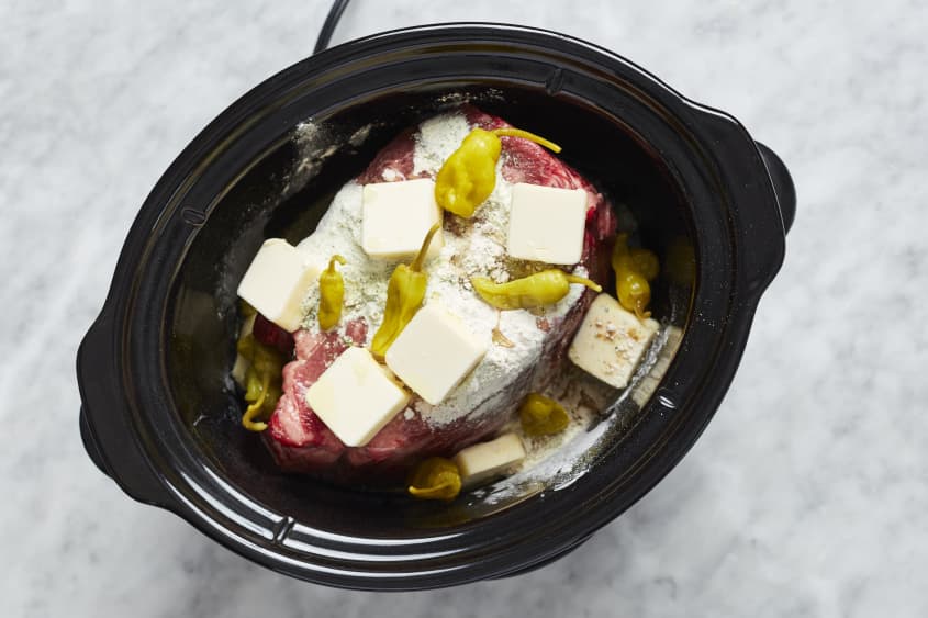 The raw pot roast is topped with dressing powders, butter, and peppers.