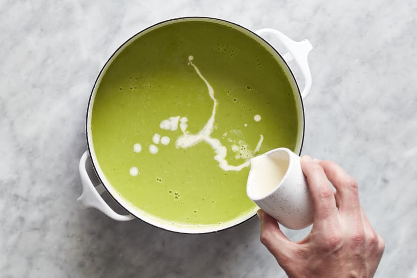 Pouring cream into asparagus soup.