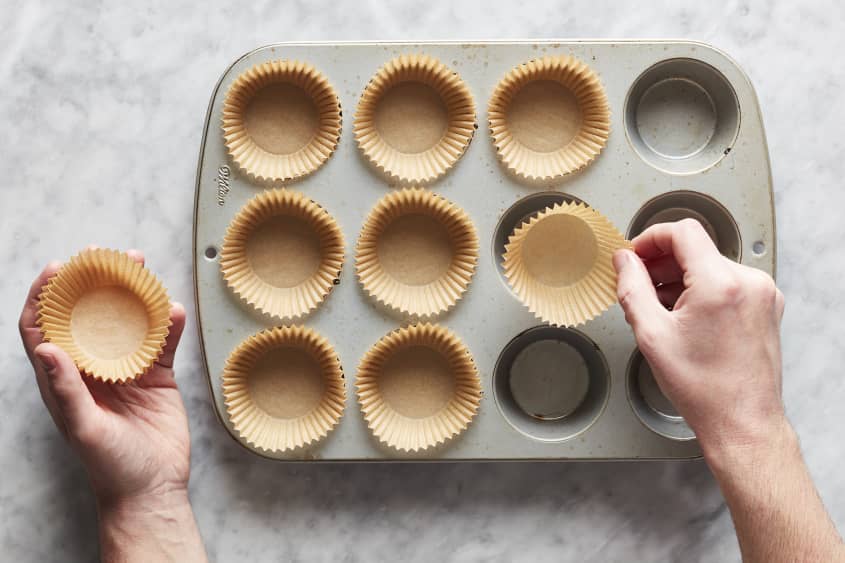 Hands lining a muffin tin with muffin liners.