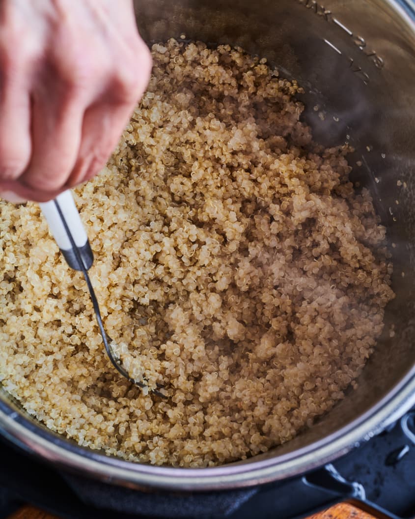 A fork is used to fluff the cooked quinoa in an instant pot.