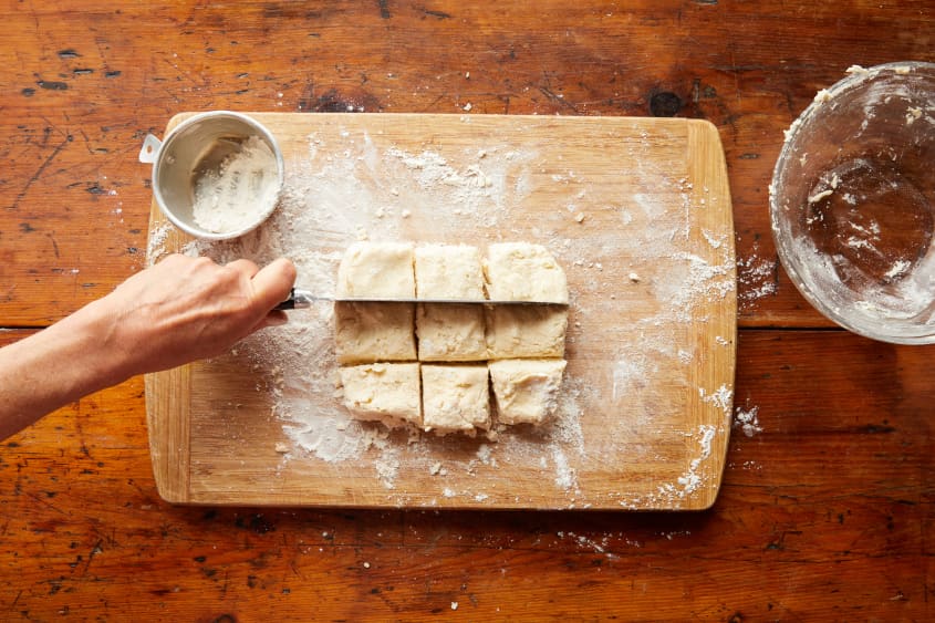 Using a knife, a hand cuts the square dough into 9 smaller squares.
