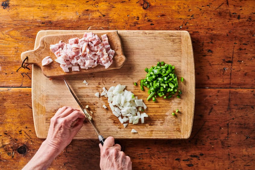 Wooden chopping board with diced onion, diced green pepper and diced uncooked bacon placed on a smaller wooden chopping board