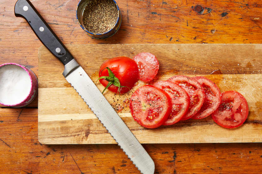 Sliced tomato on wooden cutting board, seasoned with salt and pepper