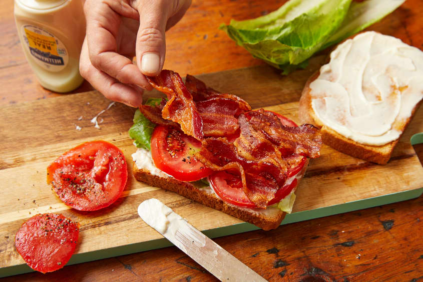 Someone assembling BLT sandwich, placing bacon on top