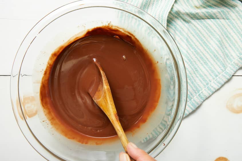 Glass bowl of melted chocolate with wooden spoon stirring chocolate