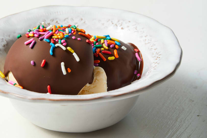 Vintage white bone ceramic bowl filled with two scoops of vanilla ice cream topped with chocolate magic shell and multi-colored sprinkles