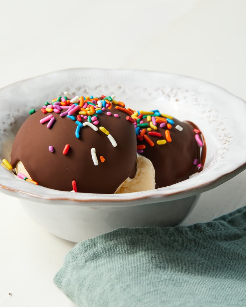 White vintage bowl filled with two scoops of vanilla ice cream topped with set magic shell and sprinkles