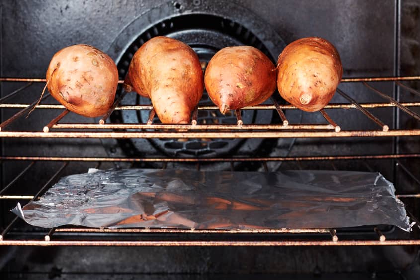 Four sweet potatoes on oven baking rack.