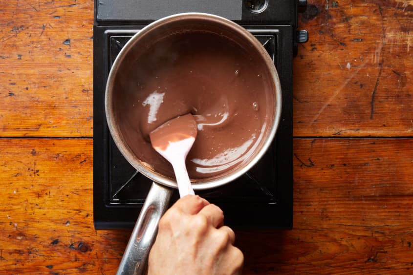 Someone stirring thickened hot chocolate over single burner.