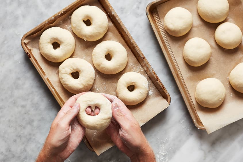 A hand creates center holes in the bagel dough.