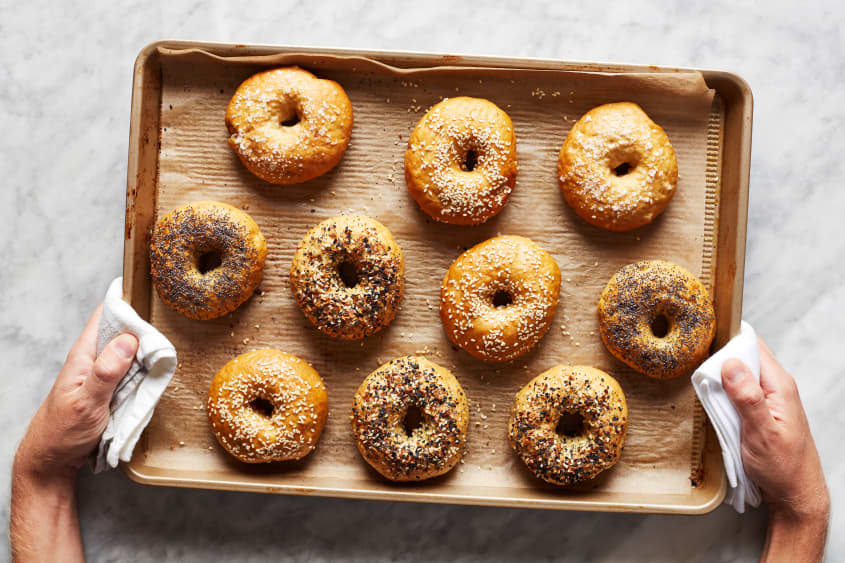 Hands holding a sheet pan of freshly baked bagels.