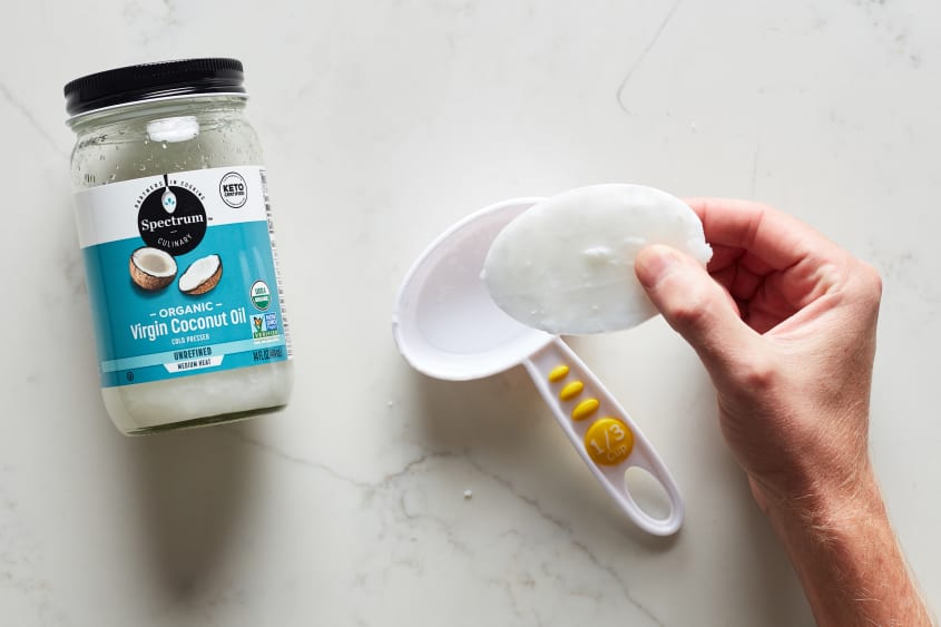 A hand picks up frozen coconut oil from inside a 1/3 cup scoop.