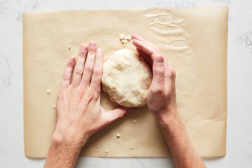 The pie dough is kneaded into a small disc.