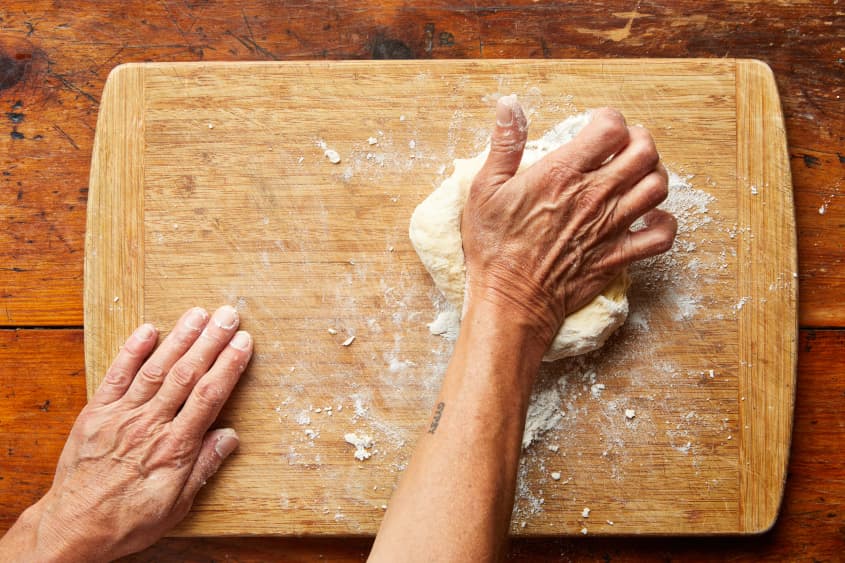Hands knead dough on a cutting board.