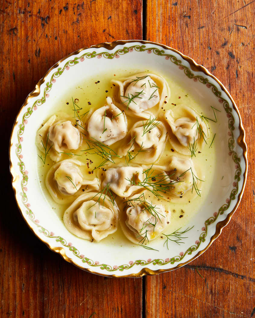 A bowl of pelmenis in broth sit on a table.