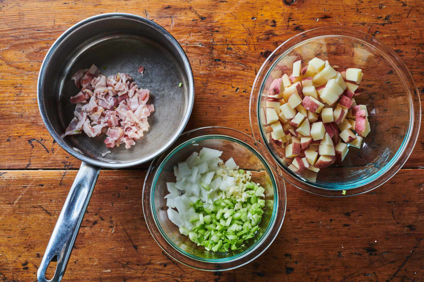 Left to right: chopped bacon in sauce pan;  diced onion, celery and garlic in glass bowl; diced potatoes in glass bowl.