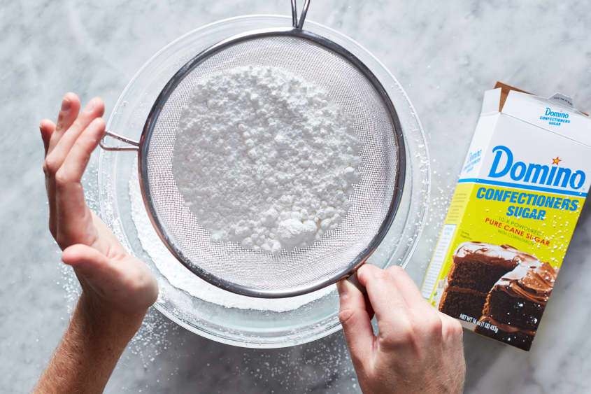 Confectioners sugar being sifted into glass bowl.
