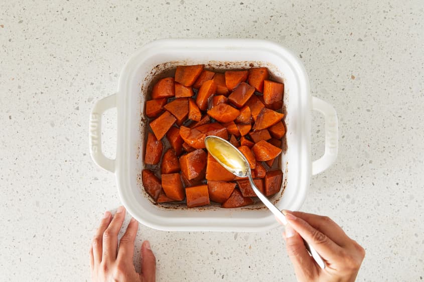 Someone placing serving spoon into baking dish with southern candied yams.