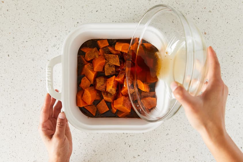 Syrup being poured over yams in baking dish.