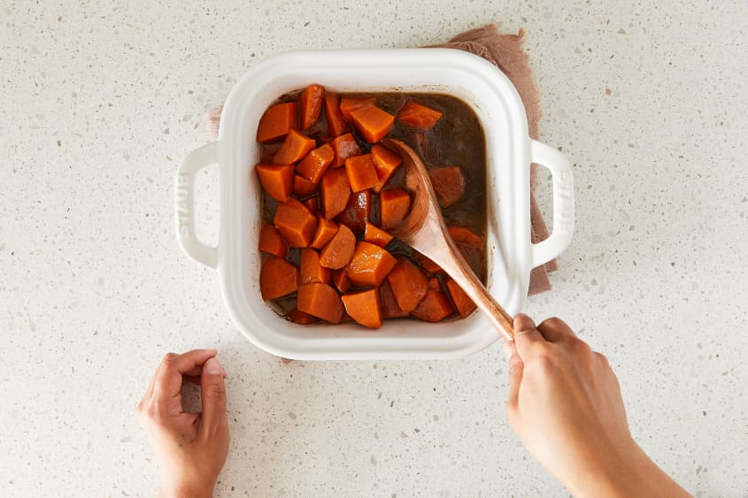 Southern candied yams being mixed in baking dish with wooden spoon.