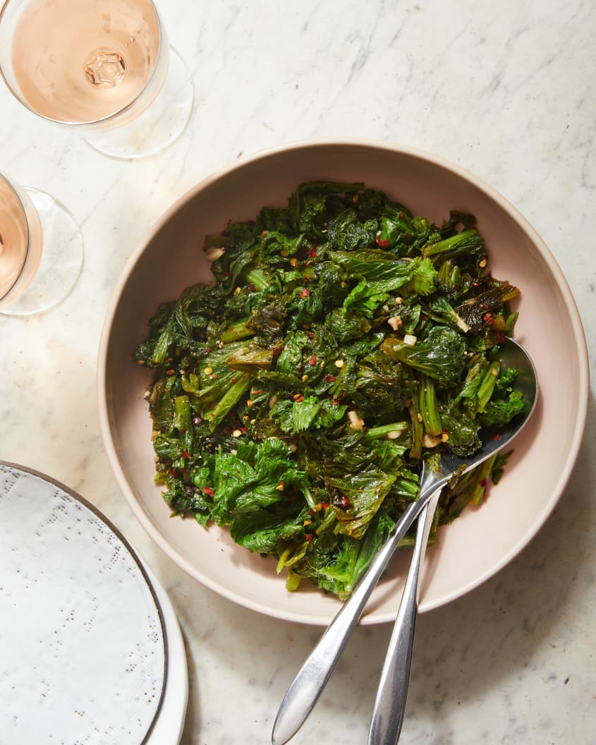 Sautéed mustard greens in side dish with serving utensils on side.