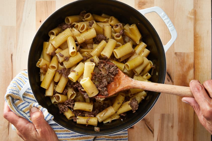Ground beef and pasta mixed in large pot with wooden spoon.