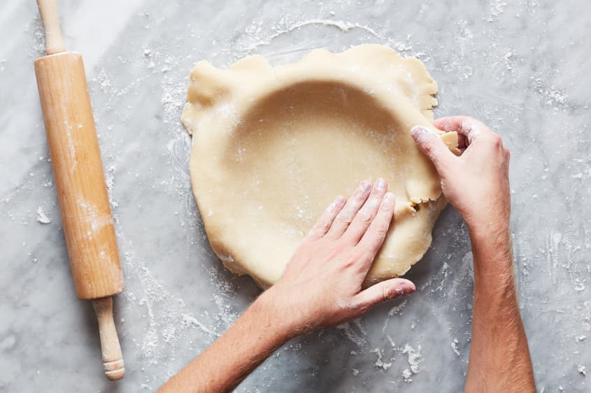 Hand patting pie dough into baking tin.