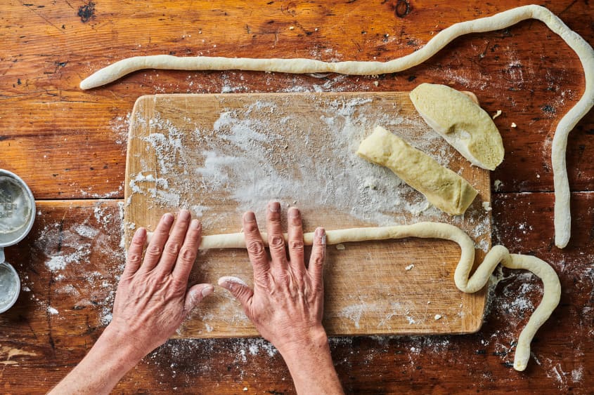Hand rolling gnocchi dough on cutting board.