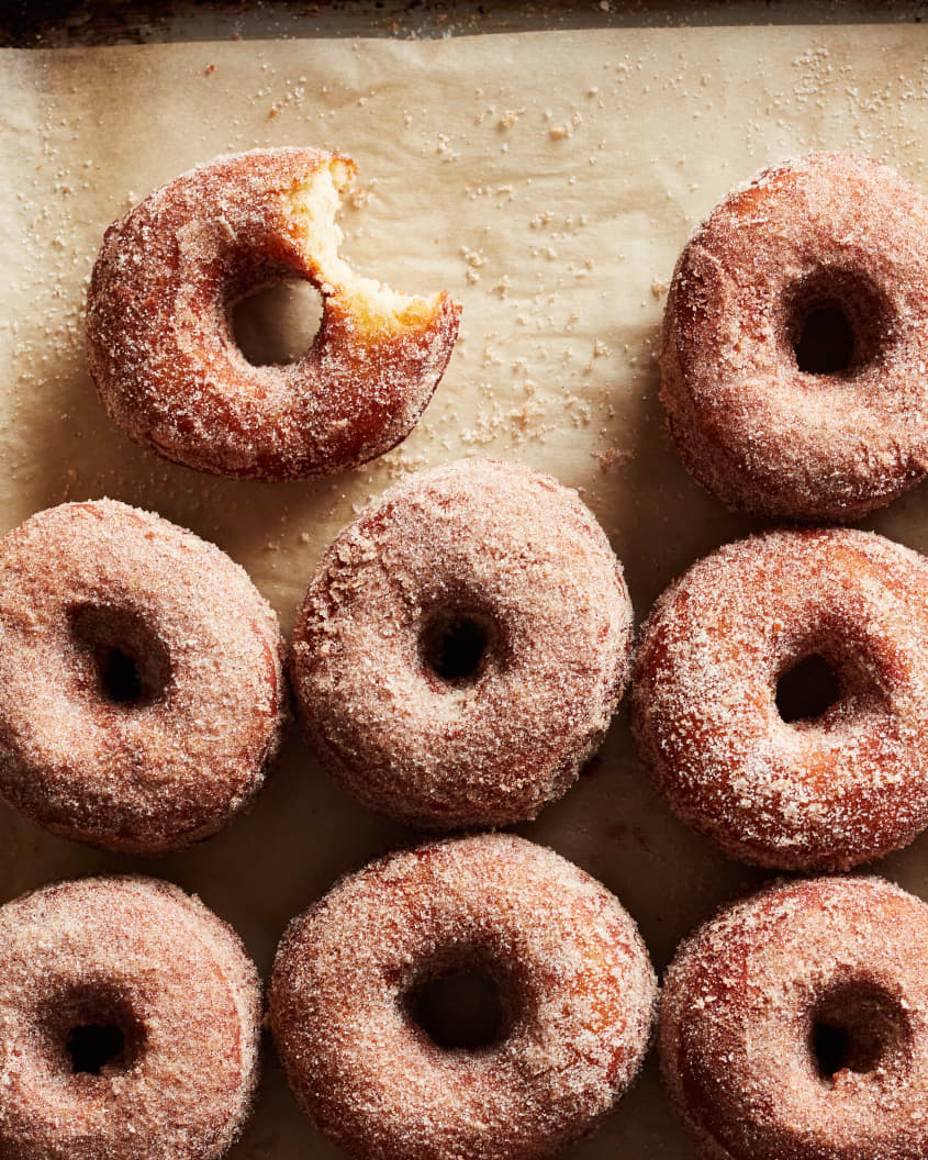 Apple cider donuts on parchment paper with one bitten.