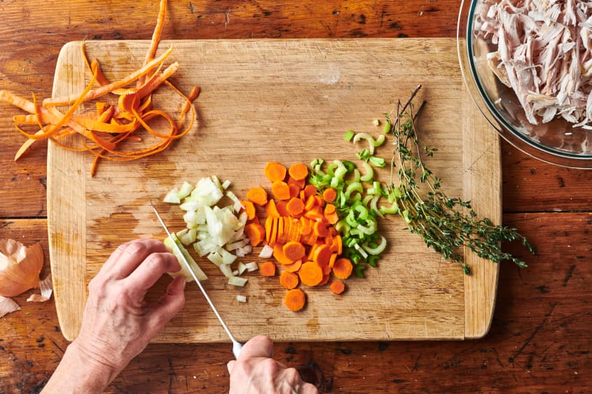 Someone chopping onion with sliced carrot, celery and thyme sprig off to the side.