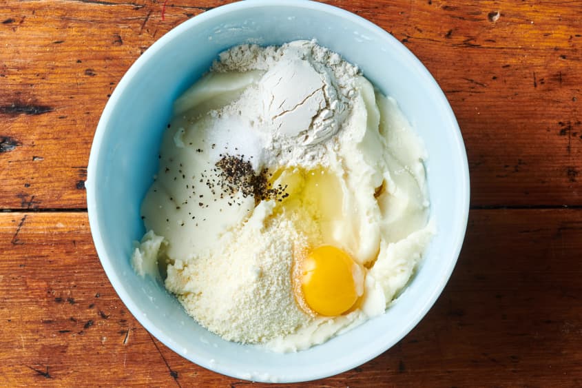 Mashed potatoes in a bowl with egg, parmesan, flour salt and pepper.