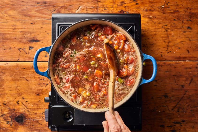 someone is stirring beef, stock, and tomatoes in a large pot with a wooden spoon