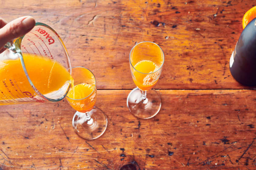 Someone pour tangerine juice into two champagne flutes.