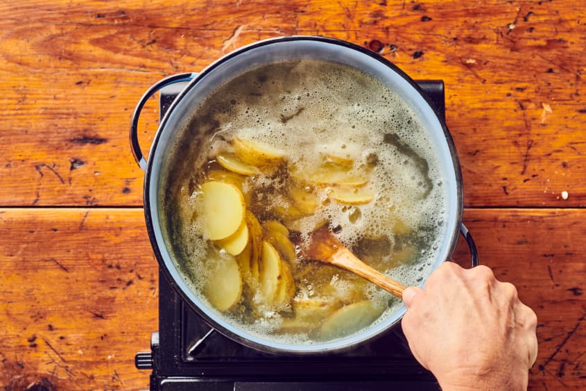 someone stirring sliced potatoes being boiled in large pot