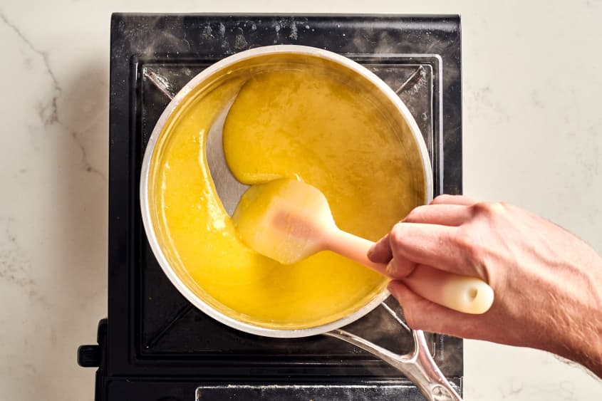 someone stirring the lemon meringue in a heated pot over a hot plate.