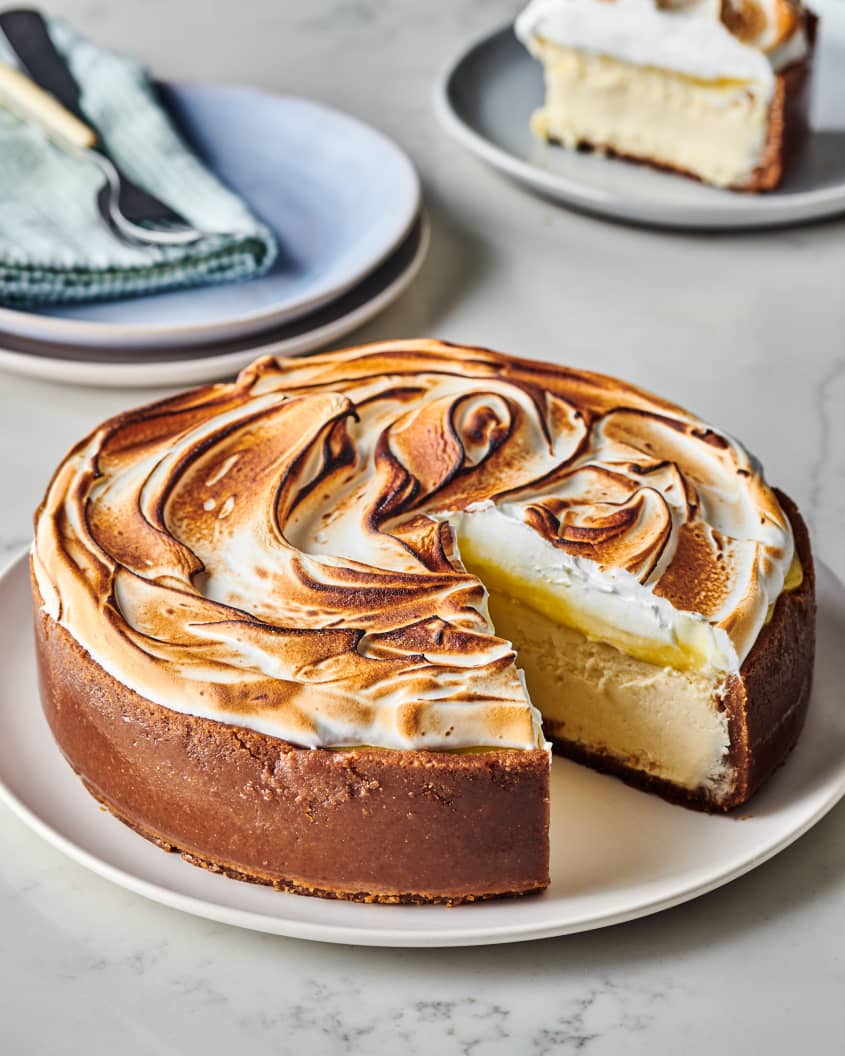 lemon meringue cheesecake sits on a plate with one slice missing from it.