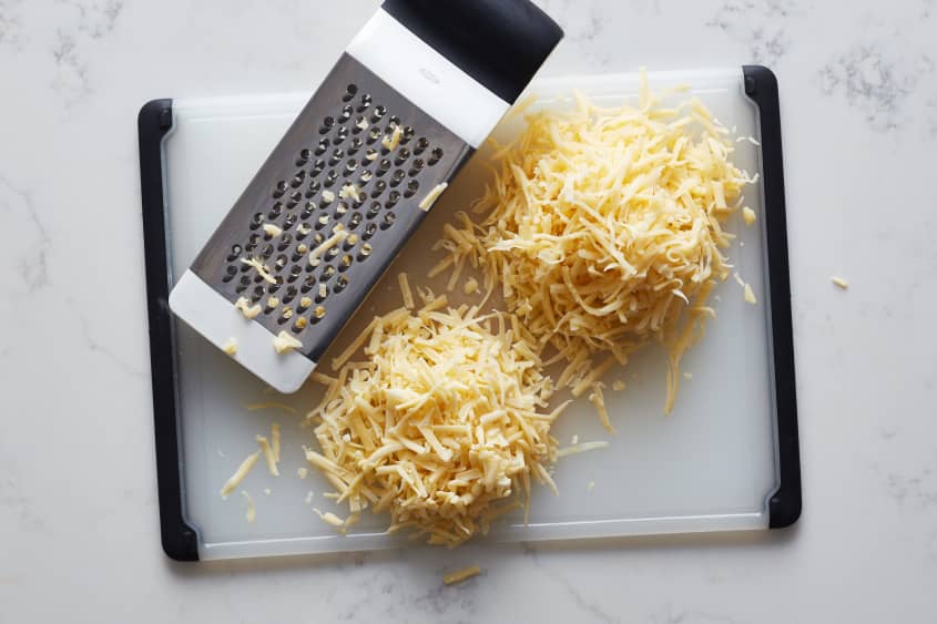 shredded cheese sits next to a cheese grater on a cutting board